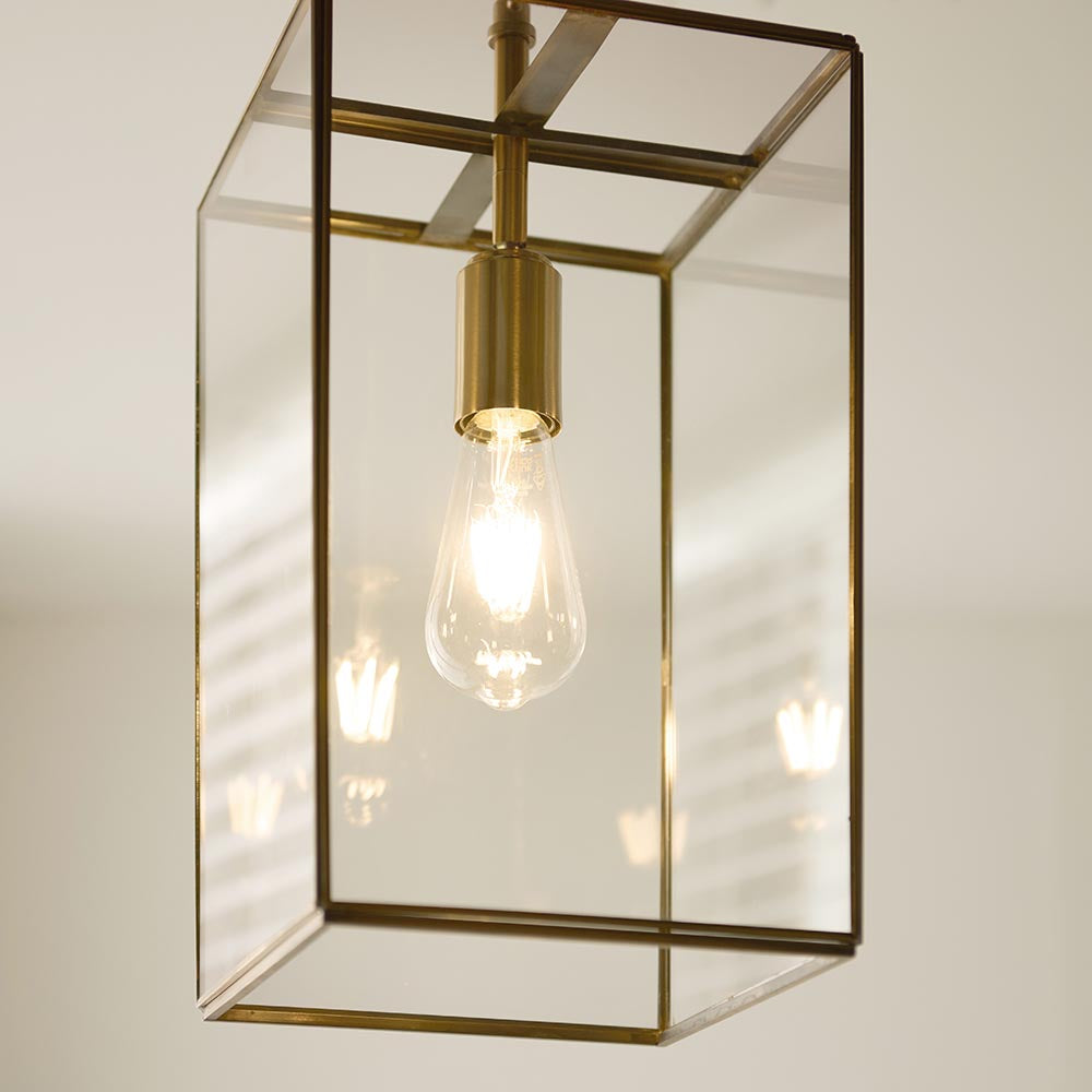 Endon Haddon Grand Pendant in brushed aged brass with clear glass panels and an exposed E27 filament bulb, shown lit against a neutral interior.