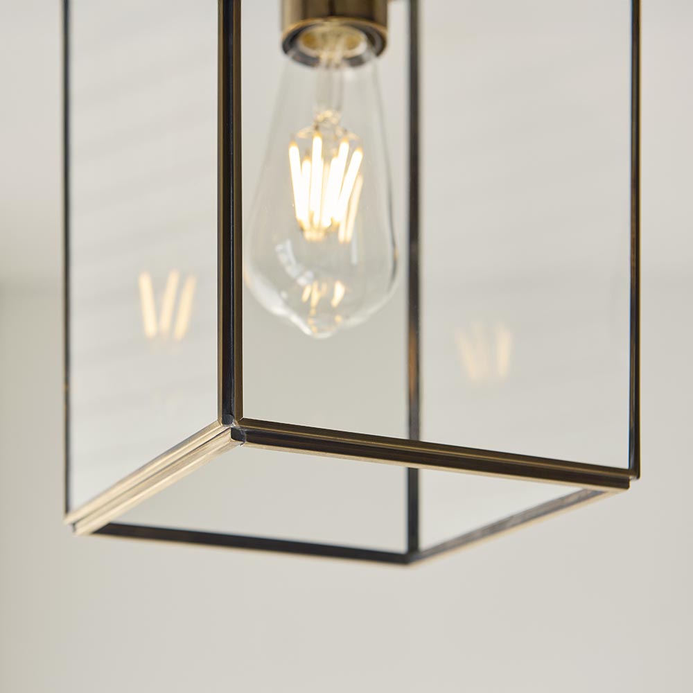 Close-up of the Haddon Pendant in brushed brass, showing the lantern-style frame with clear glass panels and an exposed E27 filament bulb.