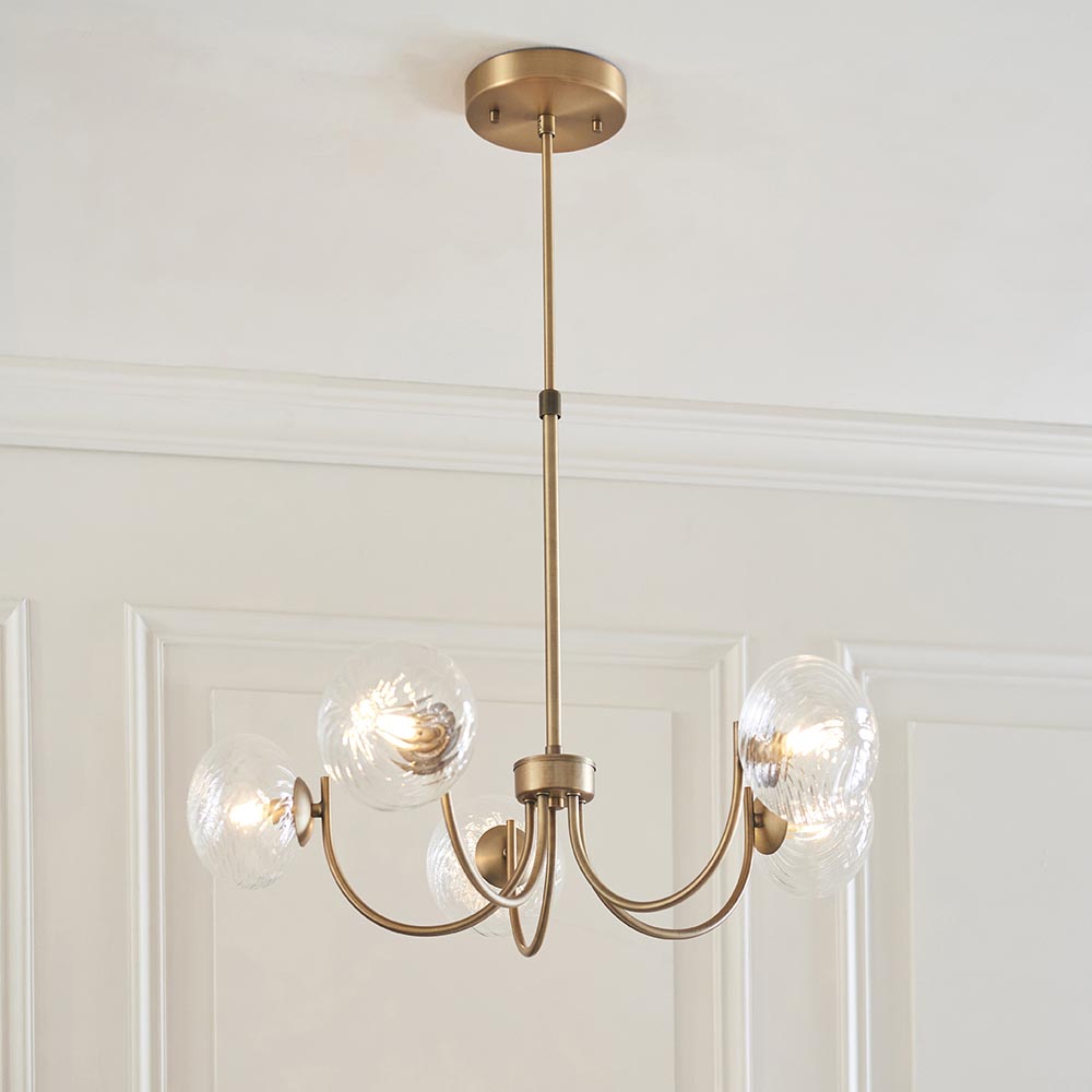 Bramwick 5 Light Pendant in antique brass with curved arms and clear twisted glass shades, shown hanging from a ceiling rose in a panelled room.