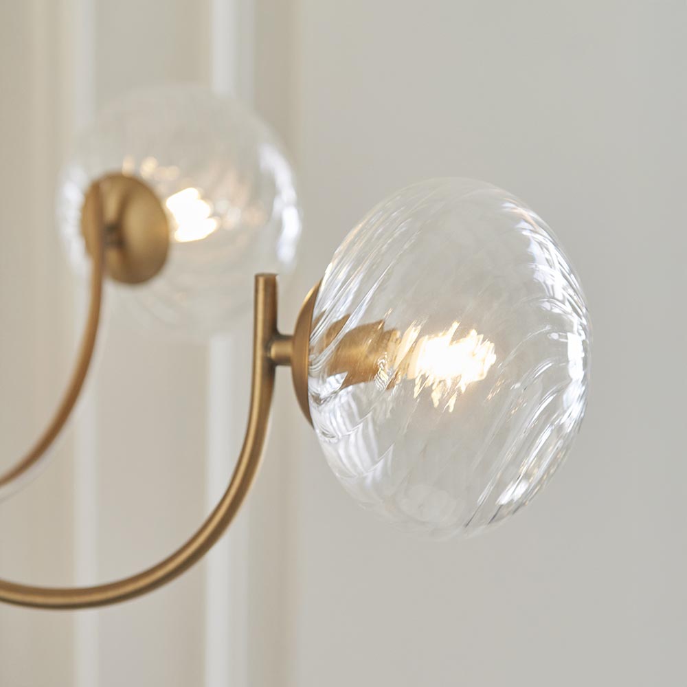 Bramwick 5 Light Pendant in antique brass, close-up of curved arms and clear twisted glass globes with G9 bulbs, plain light background.