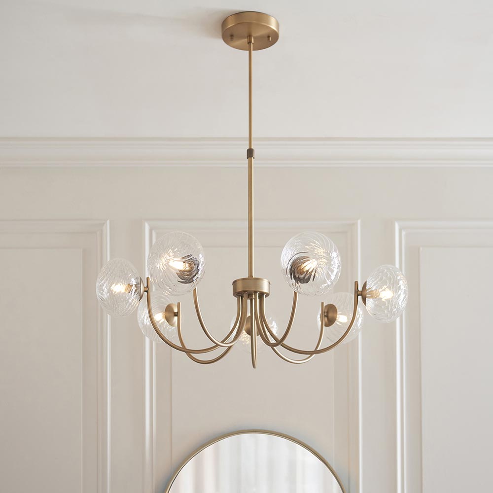 Endon Bramwick 7 light pendant in antique brass with curved arms and clear twisted glass globes, suspended from a telescopic stem above a round mirror.