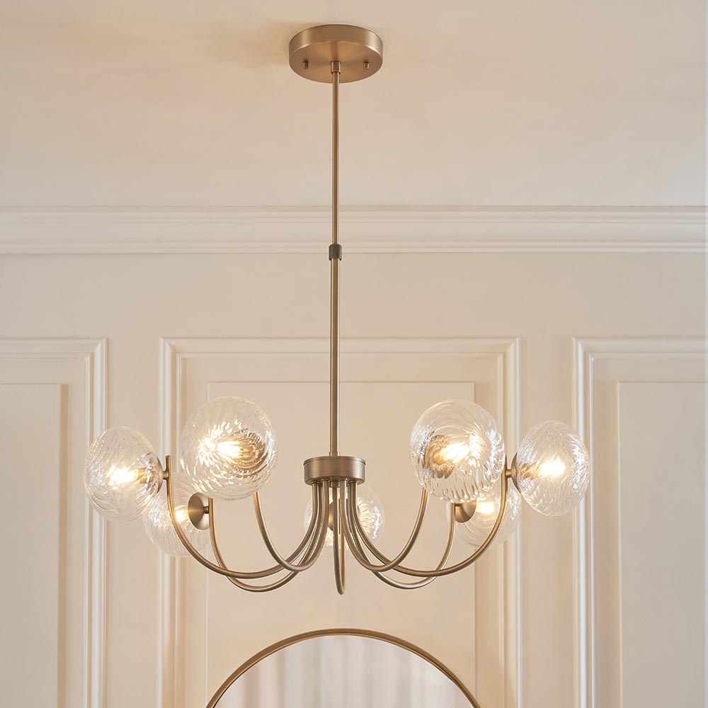 Endon Bramwick 7 light pendant in antique brass with curved arms and clear twisted glass globes, shown below a panelled ceiling above a wall mirror.