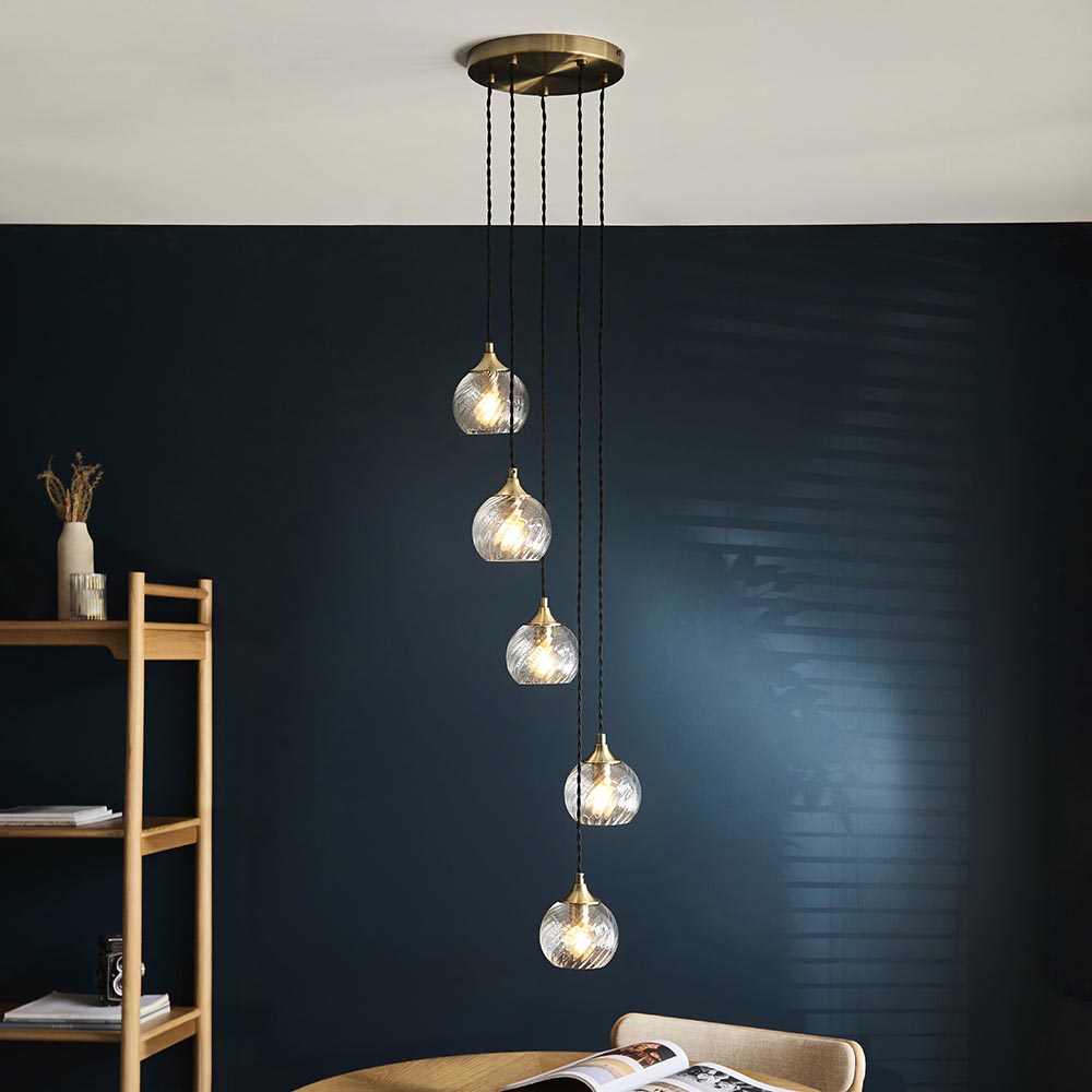 Endon Georgiana 5 light cascade pendant in antique brass with staggered spiral clear glass shades on black cables, shown in a navy dining room.