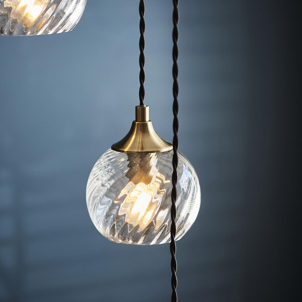 Endon Georgiana cascade pendant shade in antique brass with clear spiral glass globe and black twisted fabric cable, shown against a dark blue background.