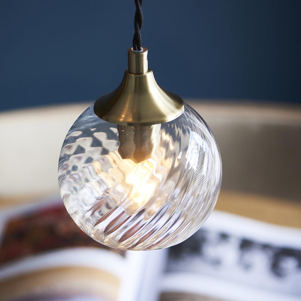 Endon Georgiana pendant light with a single clear spiral glass globe shade and antique brass fitting, suspended from a black cable against a dark blue backdrop.