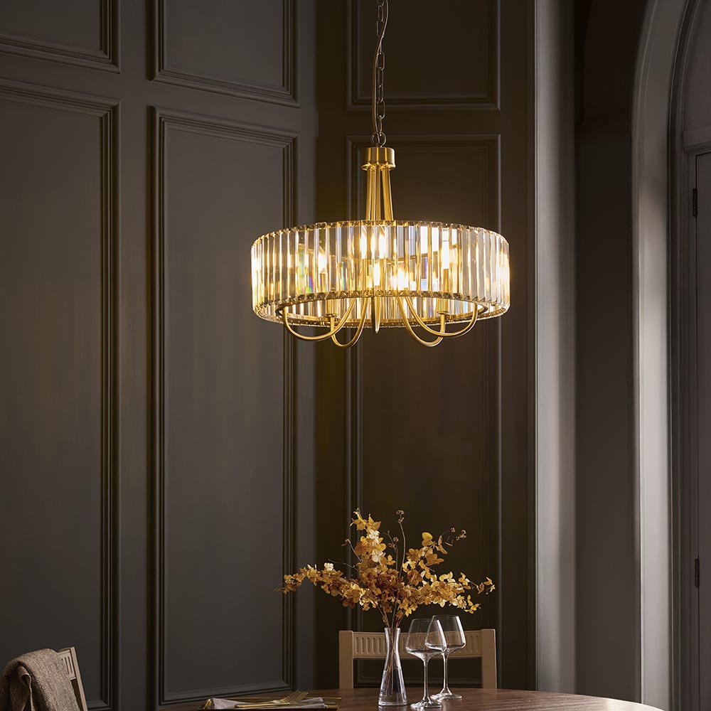 Fairfax 5 Light Pendant in antique brass with clear cut glass rods around a circular frame, shown hanging above a dining table in a dark panelled room.