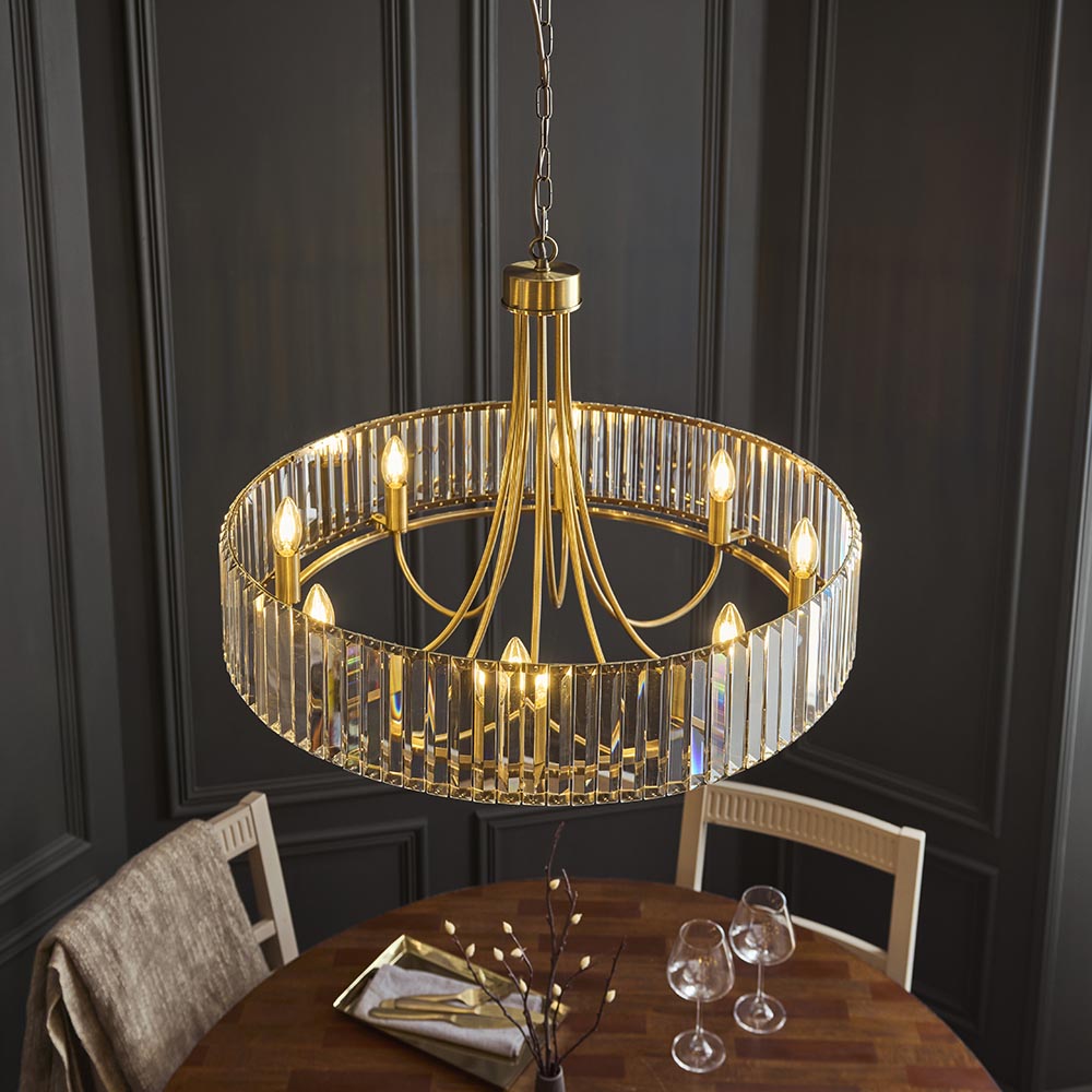 Endon Fairfax 8 Light Pendant in antique brass with a circular frame of clear cut lozenge glass, suspended above a dining table in a dark panelled room.