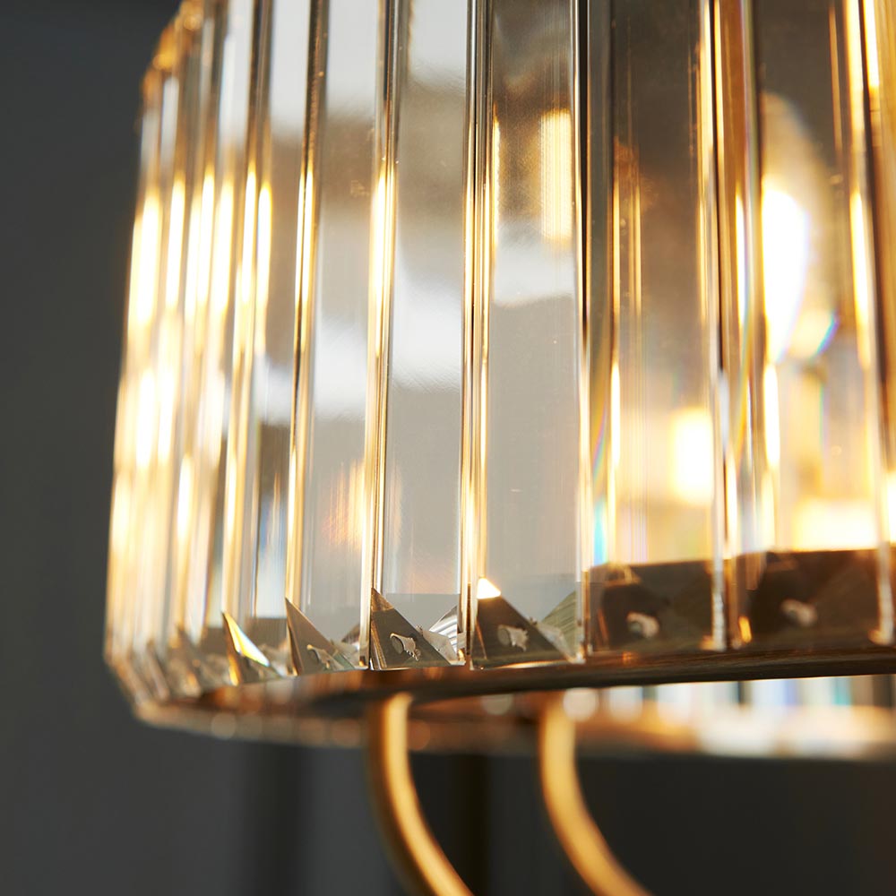 Close-up of Endon Fairfax 8 Light Pendant in antique brass, showing faceted clear cut lozenge glass panels and curved brass frame around a lit bulb.