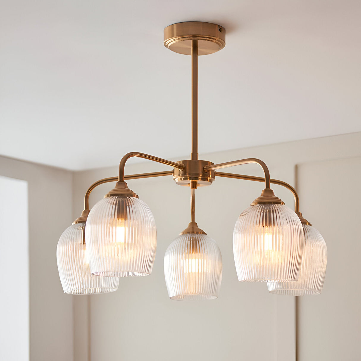 Endon Halstead Ribbed 5 light semi-flush pendant in brushed brass with fluted clear glass shades on curved arms, mounted to a white ceiling.
