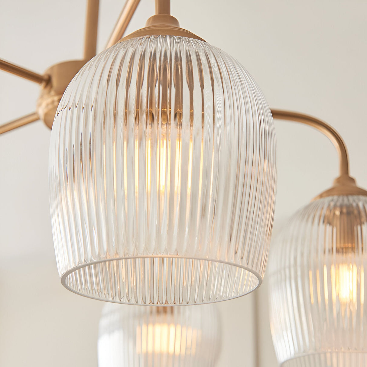Close-up of Endon Halstead Ribbed 5 Light Pendant in brass, showing fluted clear glass shades on curved arms with warm filament lamps glowing.