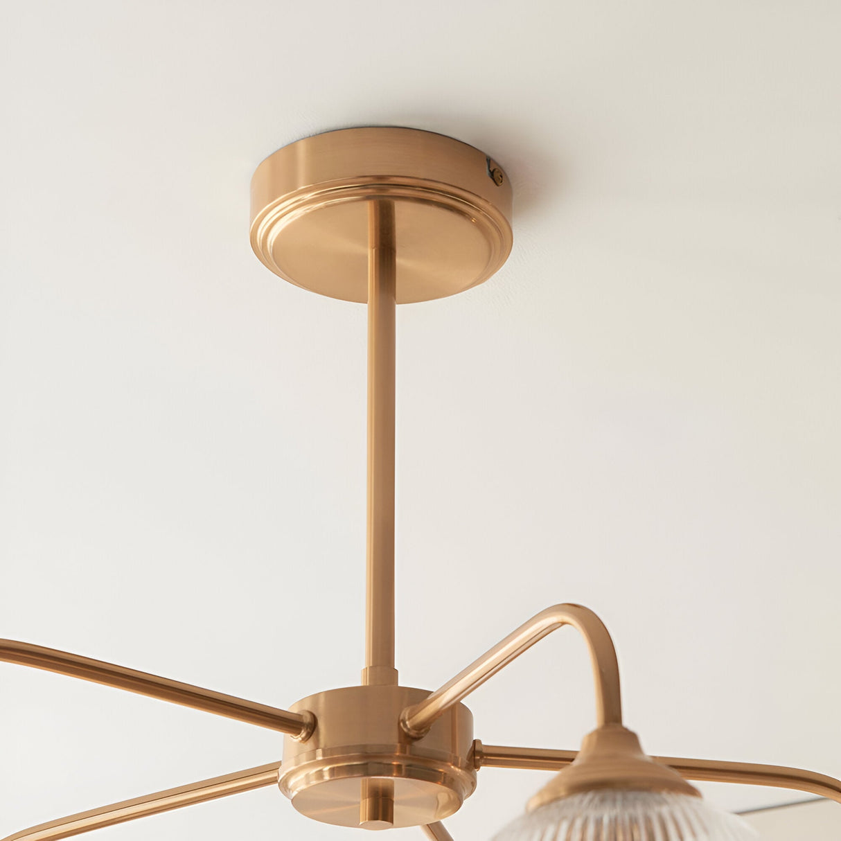 Close-up of the Endon Halstead Ribbed 5 Light Pendant ceiling rose and brushed brass stem, with curved arms extending to a fluted glass shade.