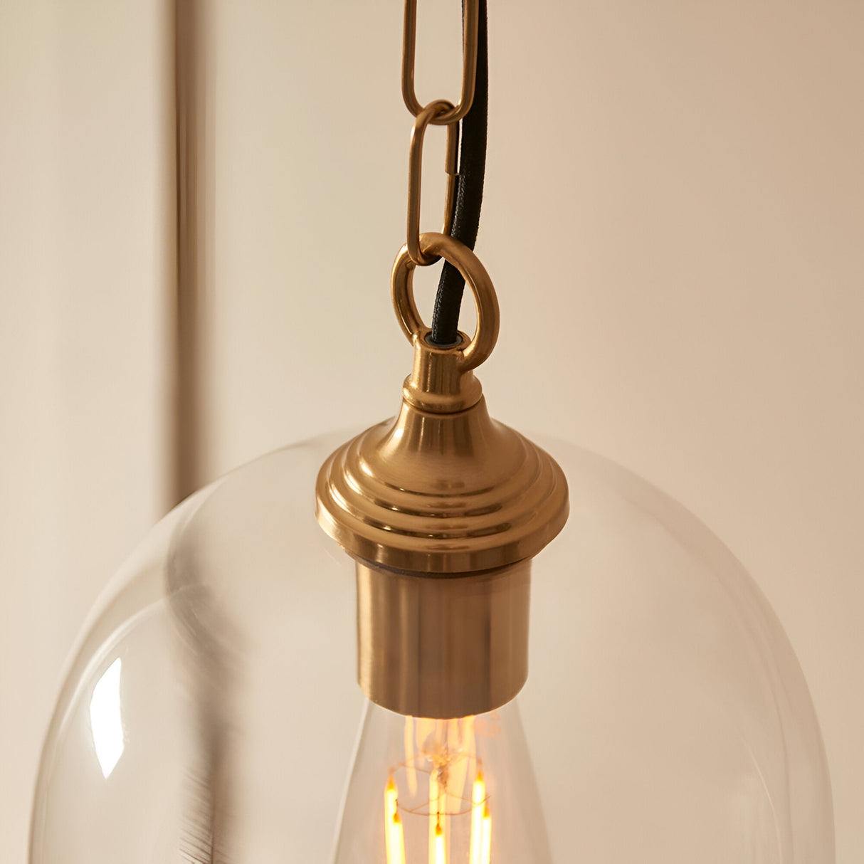 Close-up of the Halstead Pendant in brass, showing the antique brass fitting, chain link, and clear glass dome with visible bulb.