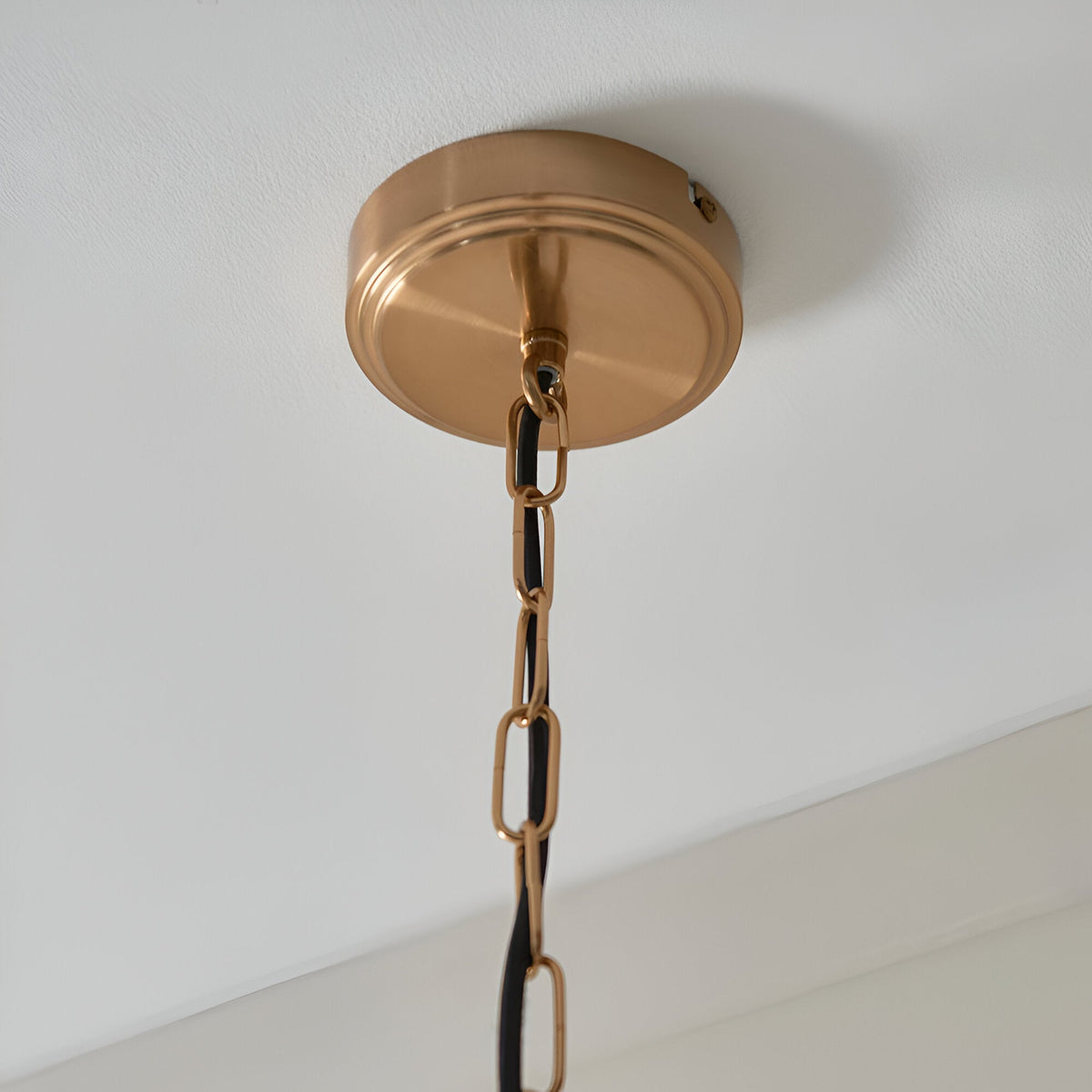 Halstead Pendant in brass shows a round ceiling rose with a brushed brass finish, linked chain, and black braided flex against a white ceiling.
