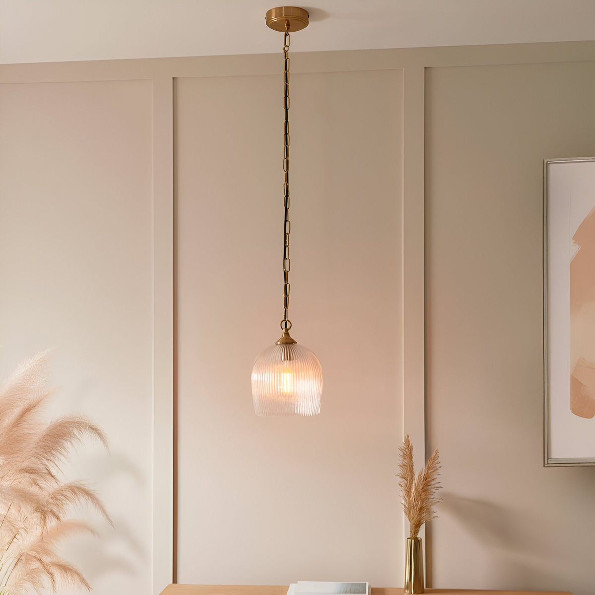 Endon Halstead ribbed single pendant with fluted clear glass dome shade and brass chain suspension, hung against a panelled beige wall above a console.