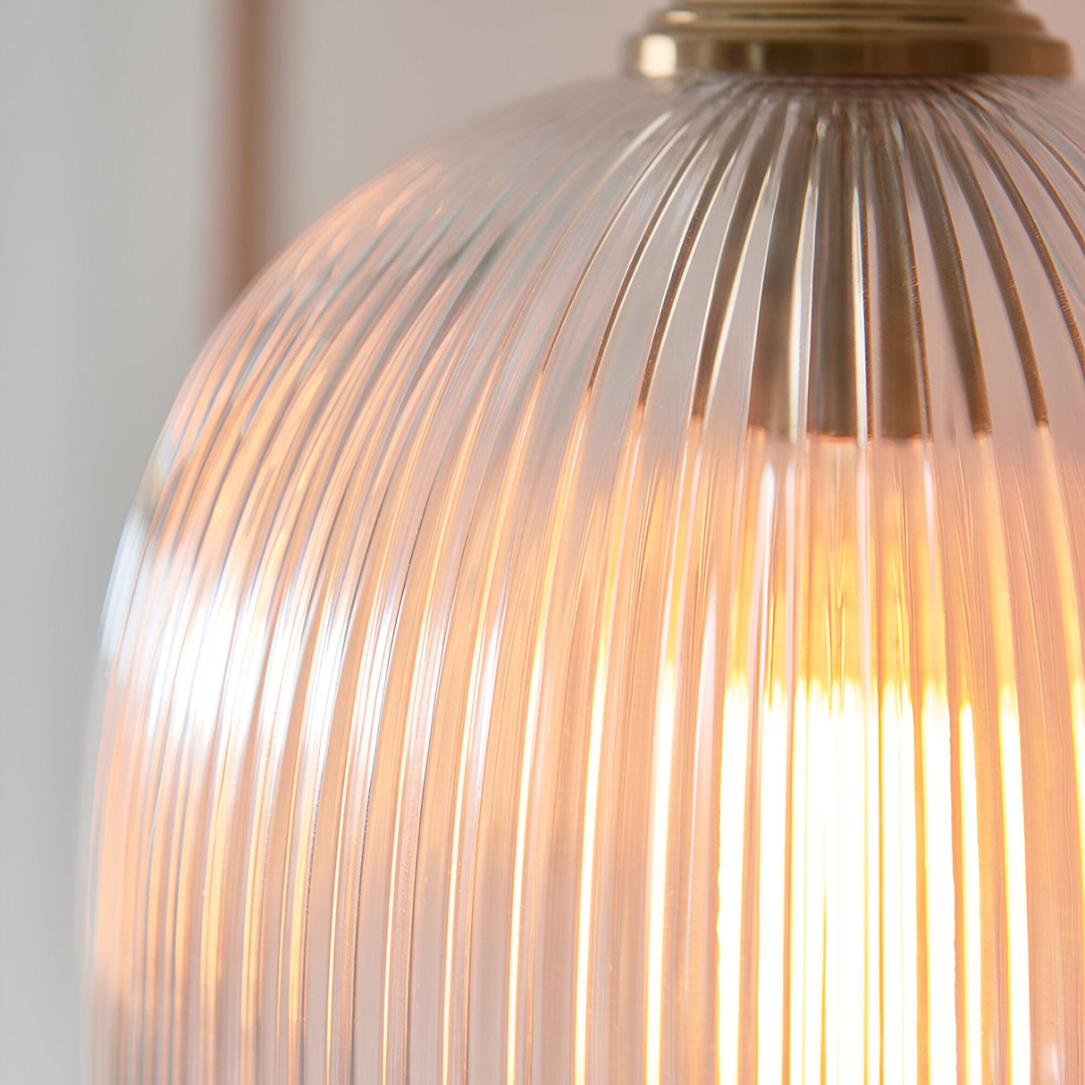 Close-up of the Endon Halstead Ribbed Pendant showing its fluted clear glass dome shade illuminated by a warm bulb, topped with a brushed brass fitting.