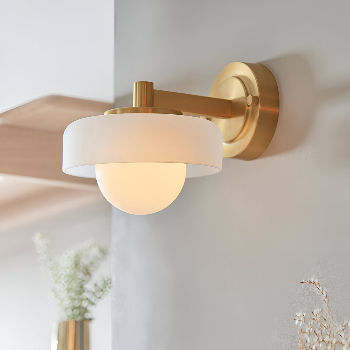 Endon Ashby wall light in brushed aged brass with a frosted glass drum shade encircling a matt opal glass sphere, mounted on a light interior wall.