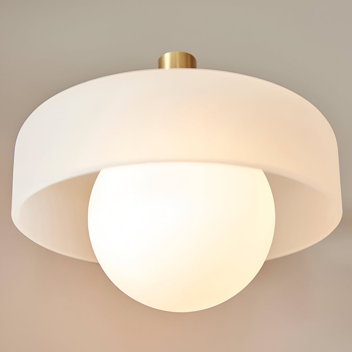 Endon Ashby wall light in brushed aged brass, with a frosted drum shade encircling a matt opal glass sphere, viewed from below.