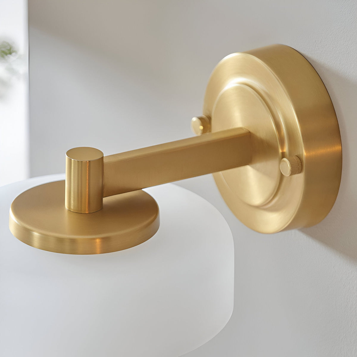 Close-up of the Endon Ashby brushed brass wall light showing the circular backplate, adjustable arm, and top of the frosted glass shade.