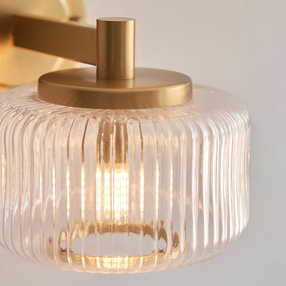Close-up of the Endon Rutland brass wall light showing the ribbed clear glass shade, brushed aged brass trim and illuminated G9 bulb within.