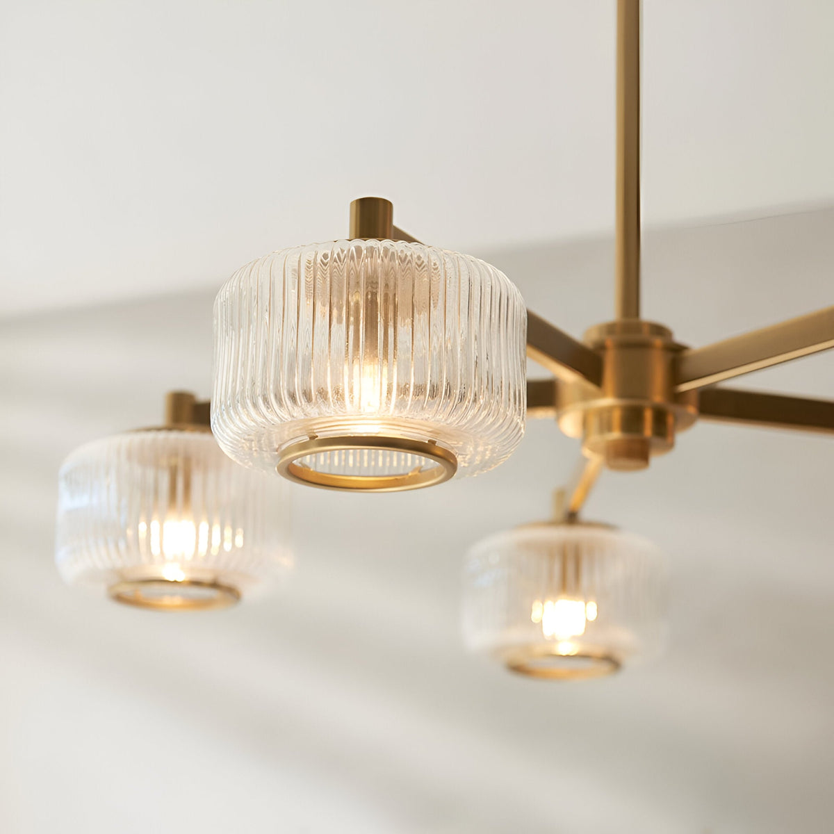 Rutland 5 Light Pendant in brushed aged brass, with clear ribbed glass shades and brass trim rings, shown close-up against a light background.