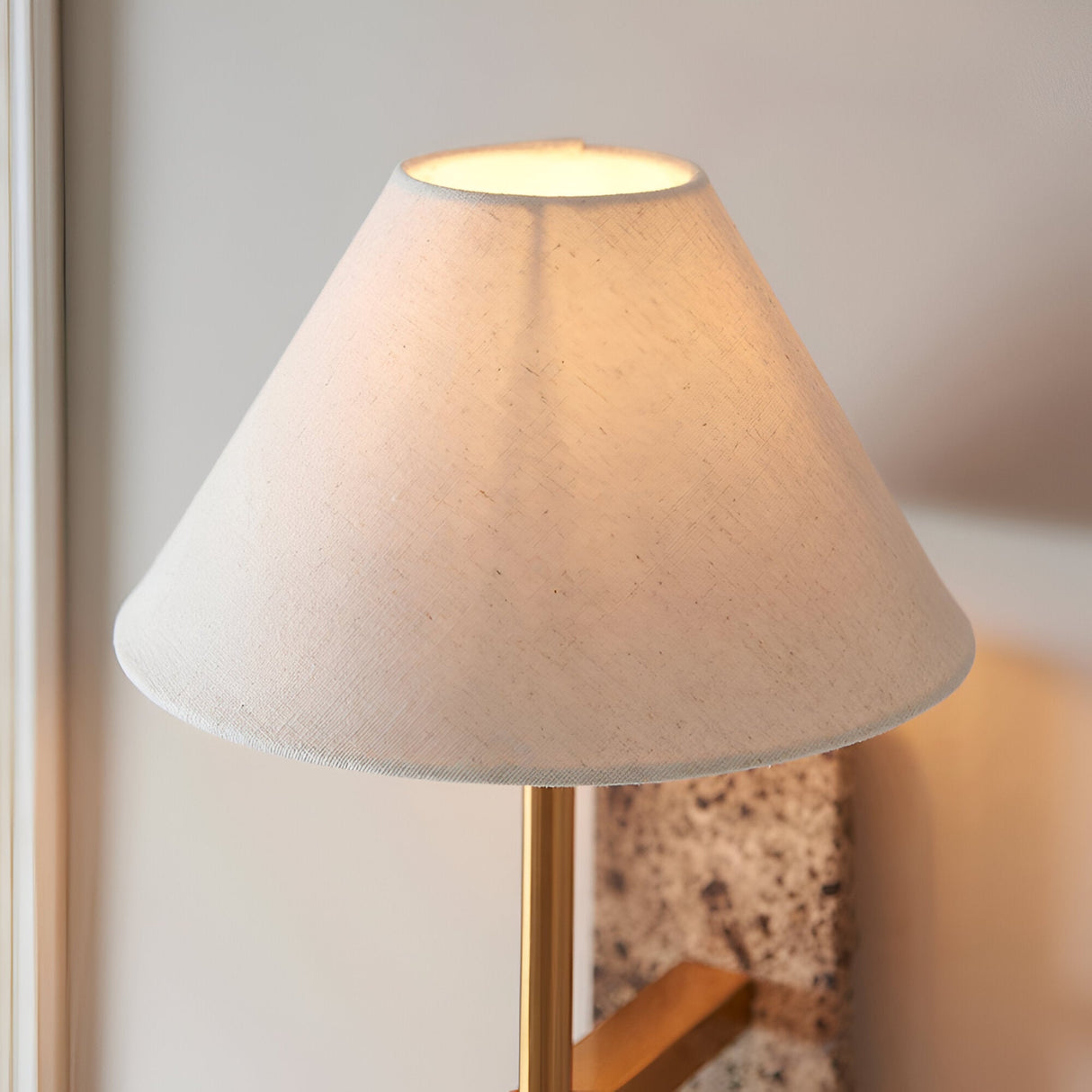 Bramble wall light with a tapered white fabric shade, brass-toned arm and natural stone backplate, mounted on a light wall.