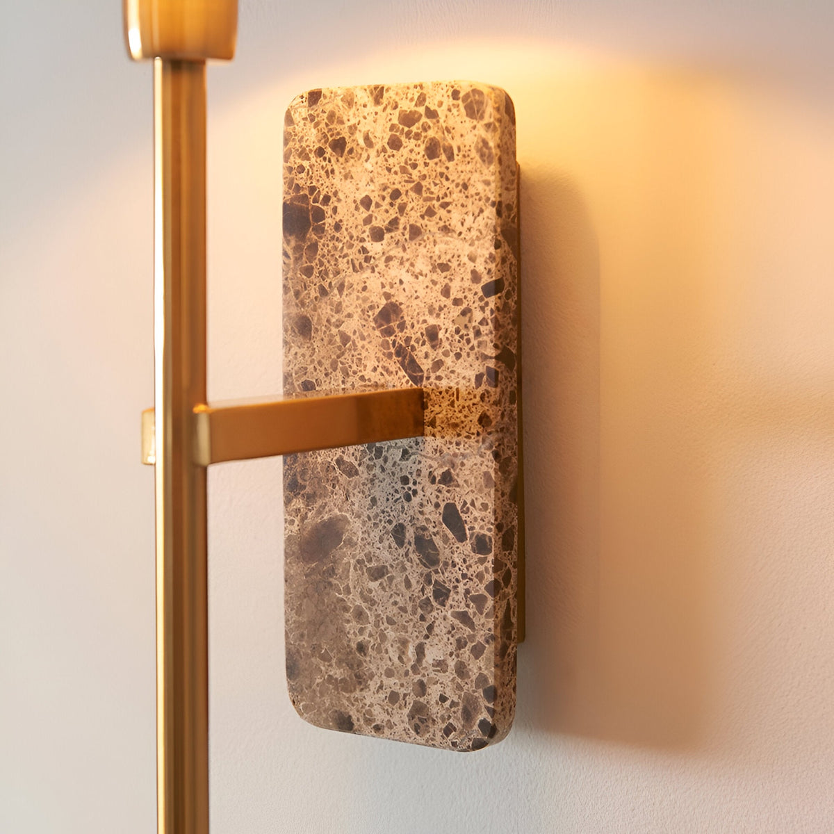Bramble Wall Light with mottled stone backplate and brass arm, mounted on a light wall showing a warm ambient glow.