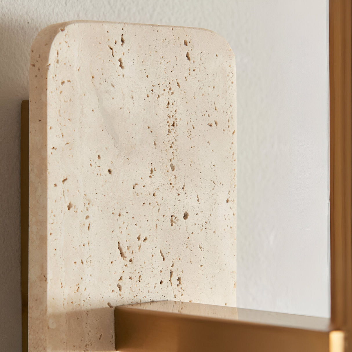 Bramble Wall Light in brass and natural stone, close-up of the textured travertine backplate with brass bracket against a plain wall.