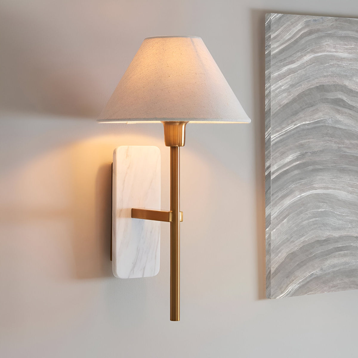 Bramble wall light with white marble backplate, brass arm, and tapered white fabric shade, shown installed on a light wall beside a marble panel.