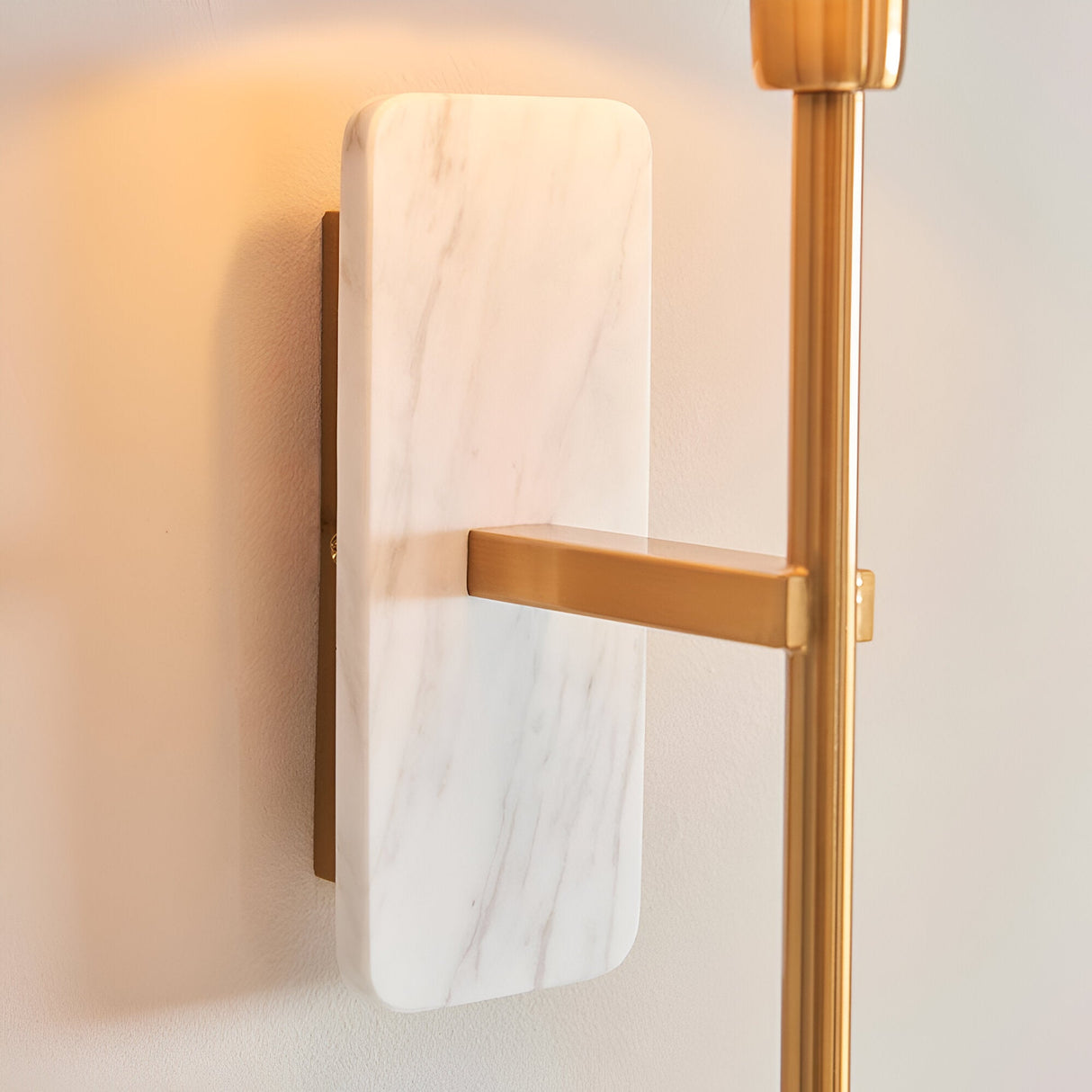 Bramble wall light with white marble backplate and brushed brass arm, mounted on a plain wall beside a matching brass floor lamp pole.