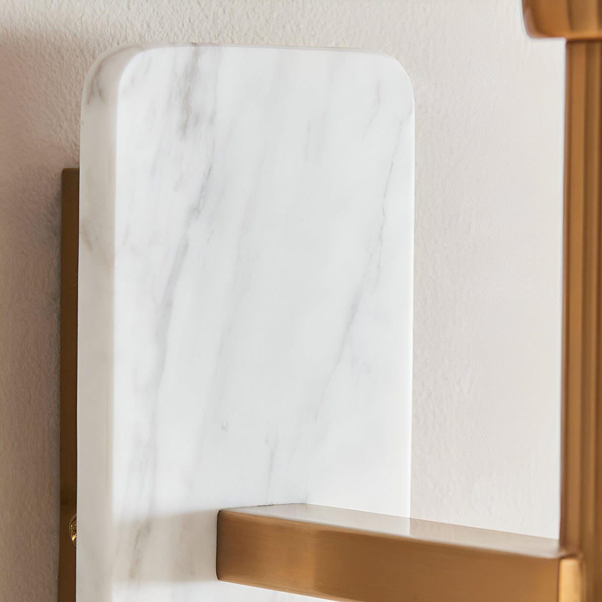Bramble Wall Light close-up showing white marble backplate with grey veining and brushed brass arm mounted on a light wall.