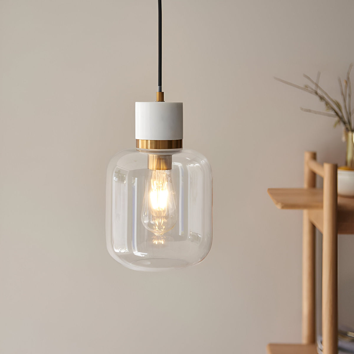 Endon Cranstead pendant light with white stone top, brushed brass collar and clear rounded glass shade with E27 filament lamp, hung near a wooden shelf.