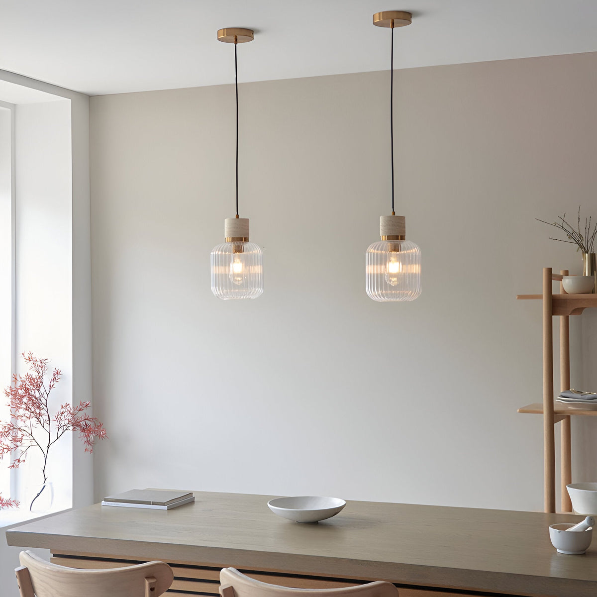 Two Cranton pendant lights with ribbed glass shades, brass collars and stone tops hang over a wooden dining table in a neutral room.