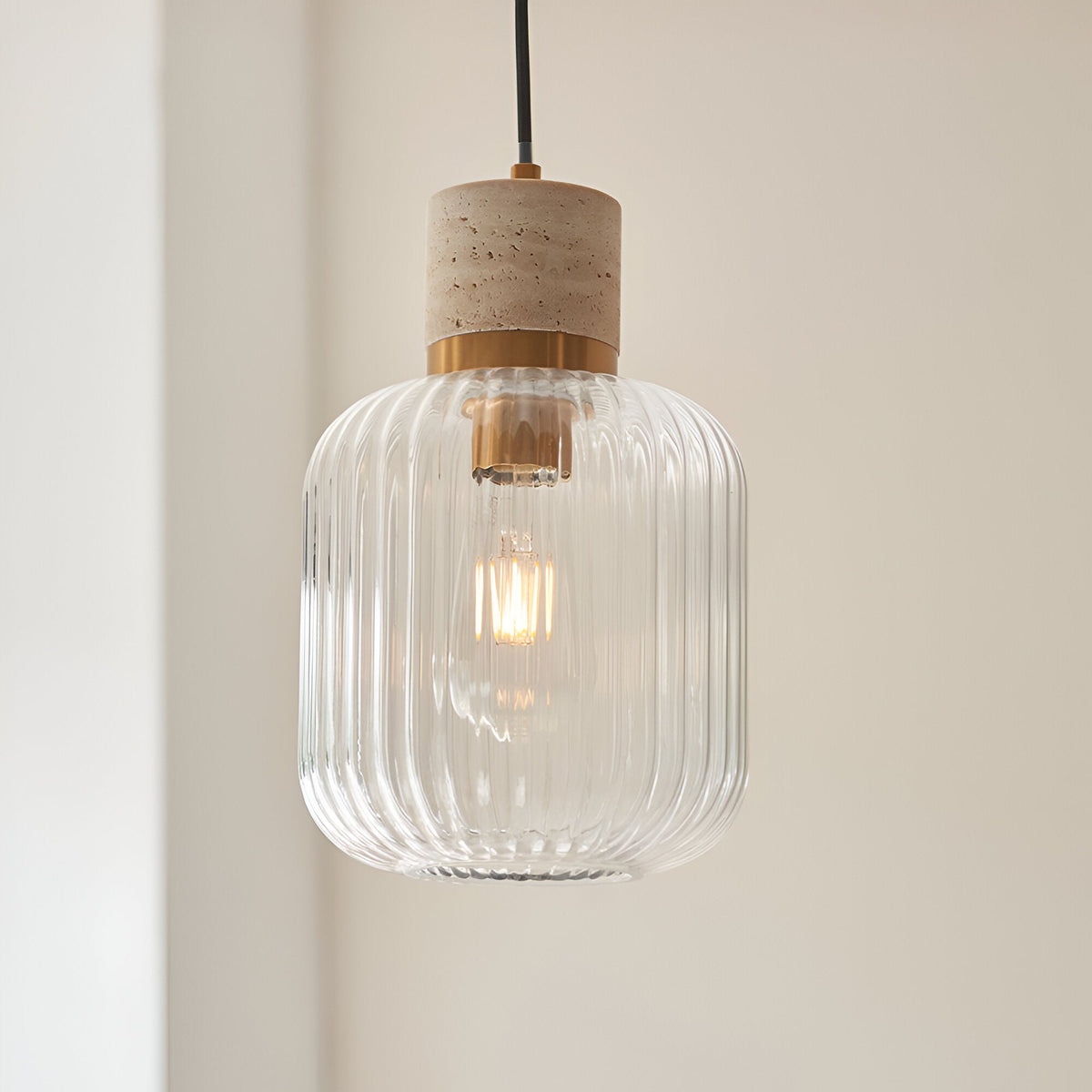 Cranton Pendant Light in brass and natural stone, with ribbed clear glass shade and black cord, hanging against a light wall.