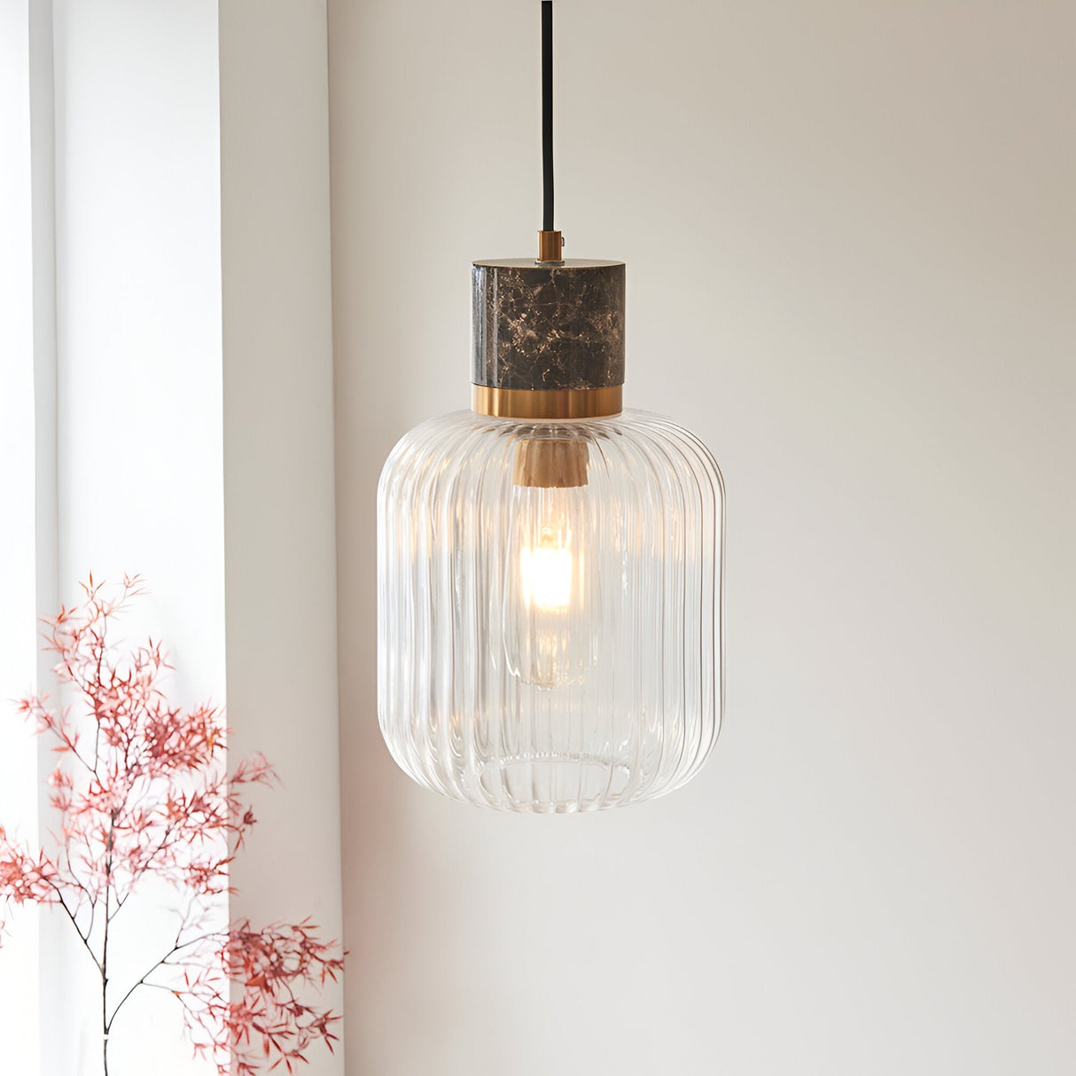 Endon Cranton pendant light with dark brown Emperador marble top, brushed brass collar and clear ribbed glass shade, hanging in a bright interior.