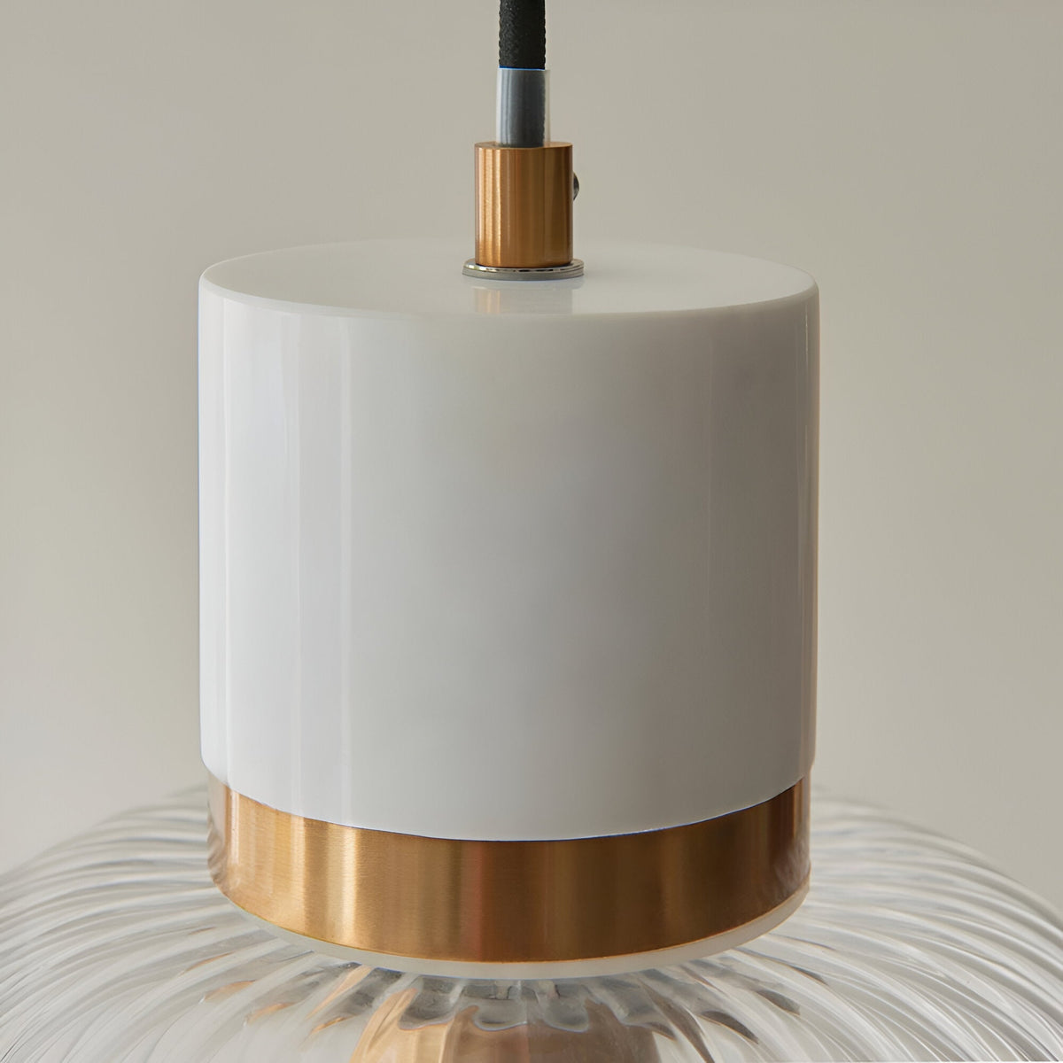 Cranton Pendant Light close-up showing white stone top, brushed brass collar, and ribbed clear glass shade with black cable, on a plain light background.