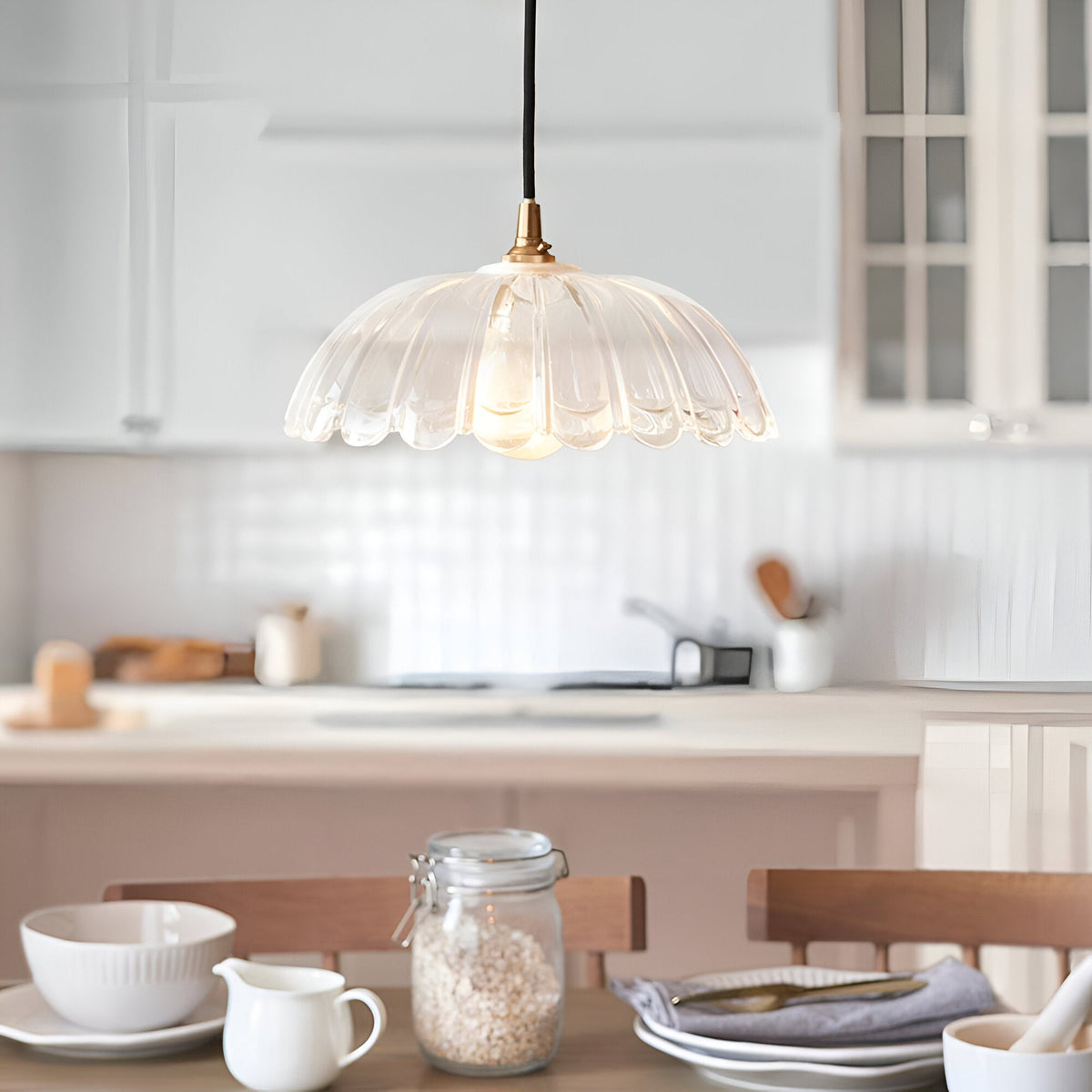Endon Brackmont Carnation pendant light with a clear scalloped glass shade and brass fitting on a black cable, hanging above a bright white kitchen island.