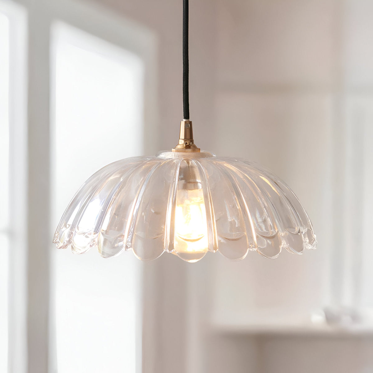 Endon Brackmont Carnation pendant light with scalloped clear glass shade and brushed brass fitting on a black braided cable, hung by a bright window.