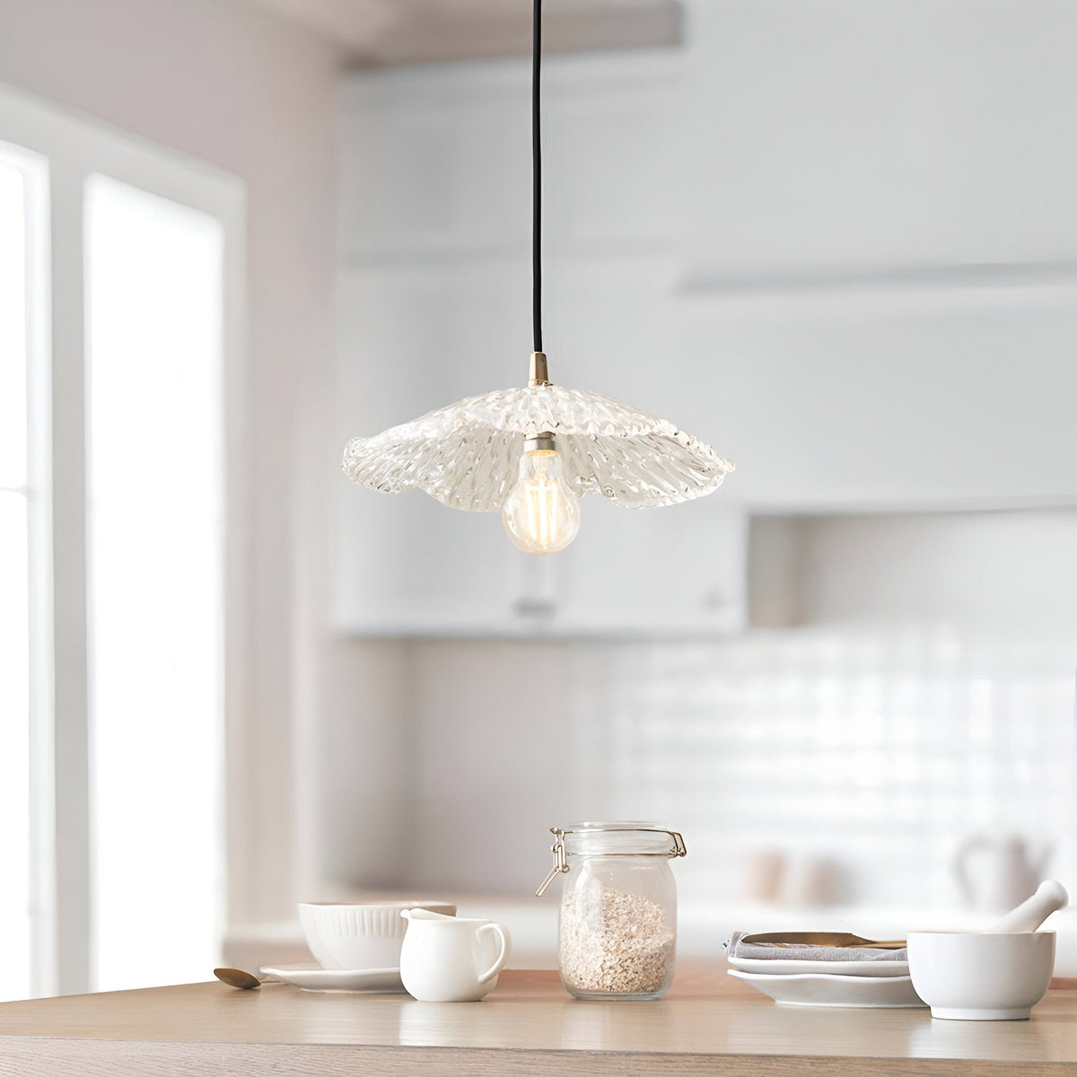 Brackmont Orchid Pendant in brass and black with a ripple-textured clear glass shade, shown lit above a kitchen island with a black braided flex.