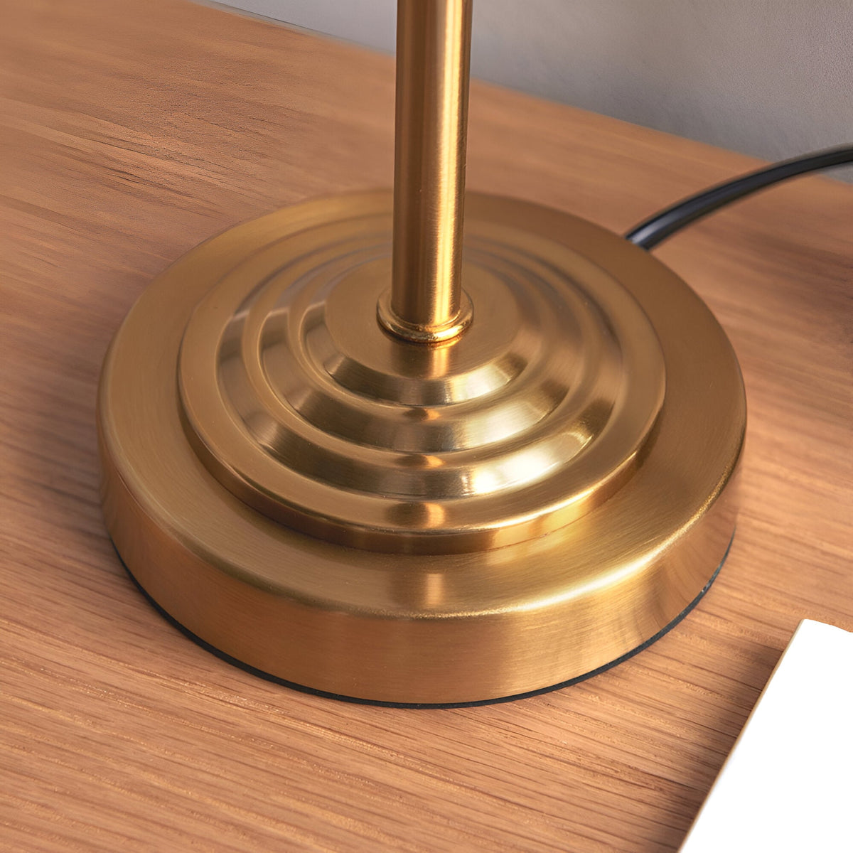 Close-up of the Cliffbourne Ivy Table Lamp's stepped brass metal base and stem on a wood surface, showing the ringed disc design and cable.
