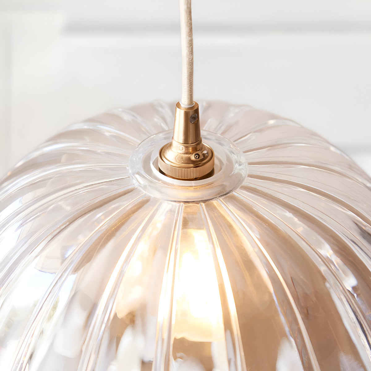 Close-up of the Endon Brackmont Carnation pendant showing the scalloped clear glass dome, brushed aged brass B22 fitting and natural braided cable.