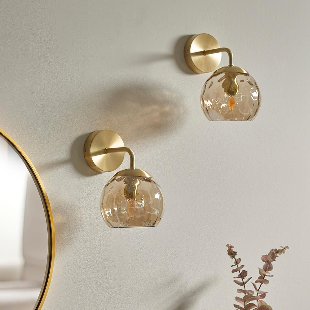Endon Draycott wall lights in satin brass with champagne dimpled glass globe shades, mounted as a pair on a pale wall beside a round gold-framed mirror.