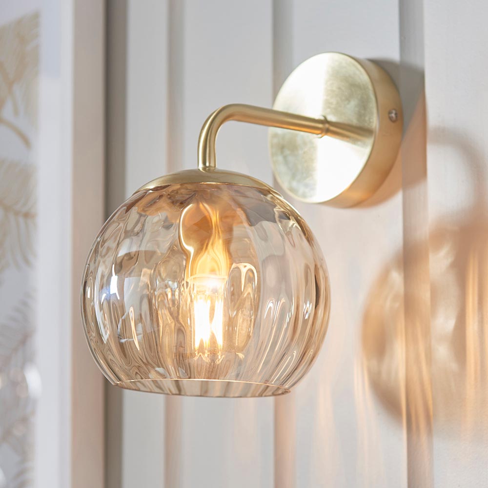 Endon Draycott wall light in satin brass with a champagne lustre dimpled glass globe shade, lit on a panelled wall beside botanical artwork.
