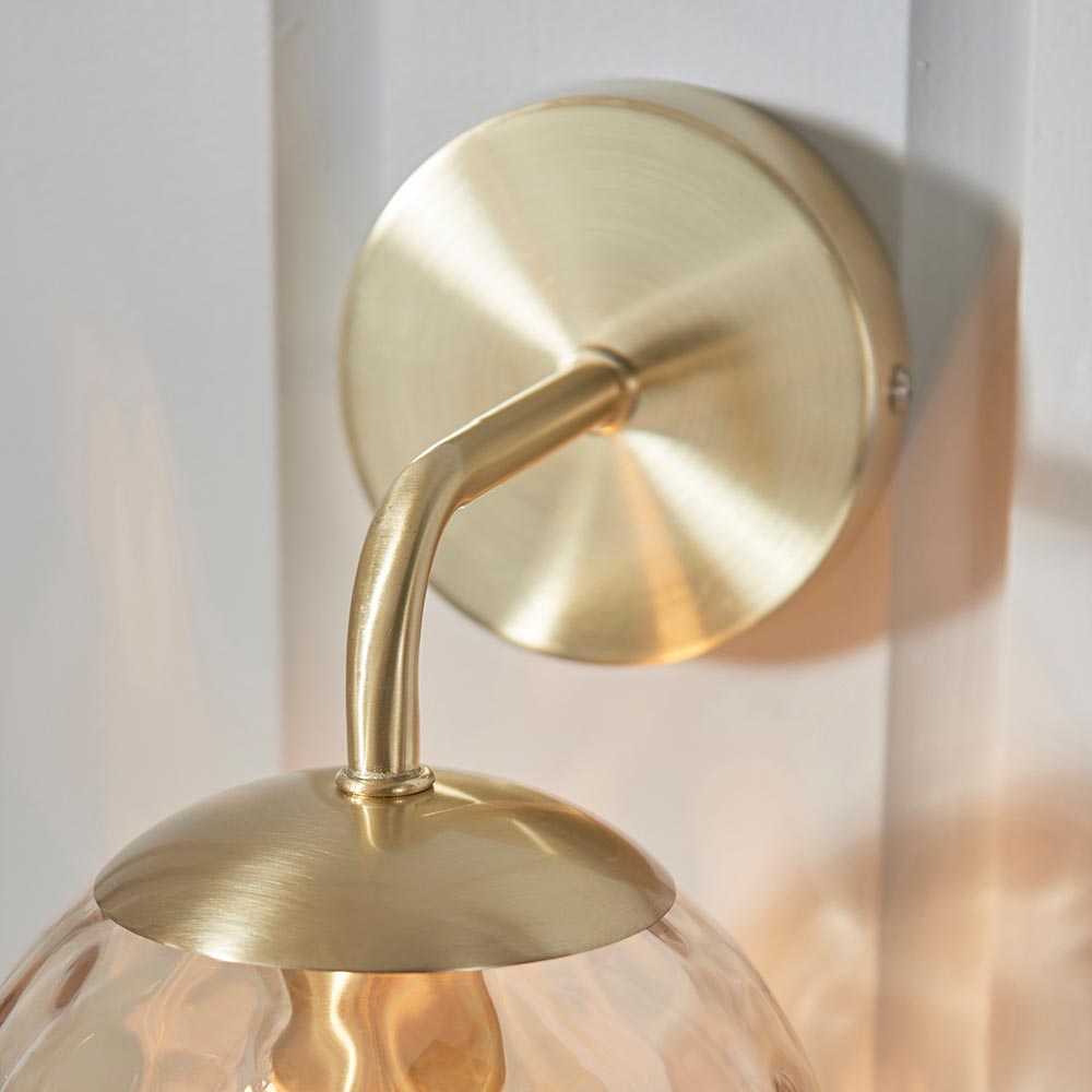 Close-up of Endon Draycott wall light showing satin brass circular back plate, curved arm, and top of champagne dimpled glass shade.