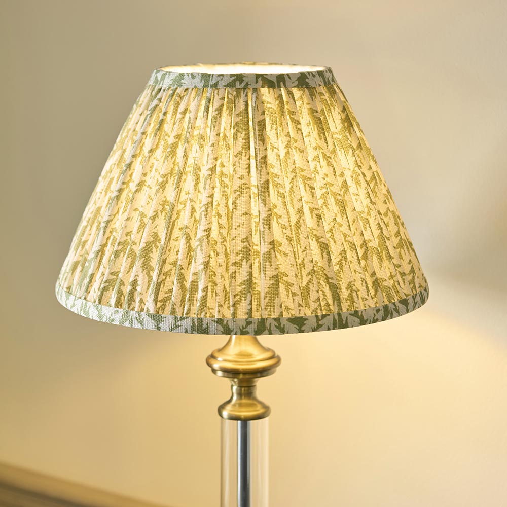 Endon Aldmont Leaf table lamp with a gathered, pleated green leaf-print faux linen shade on an antique brass cap and clear glass column base.