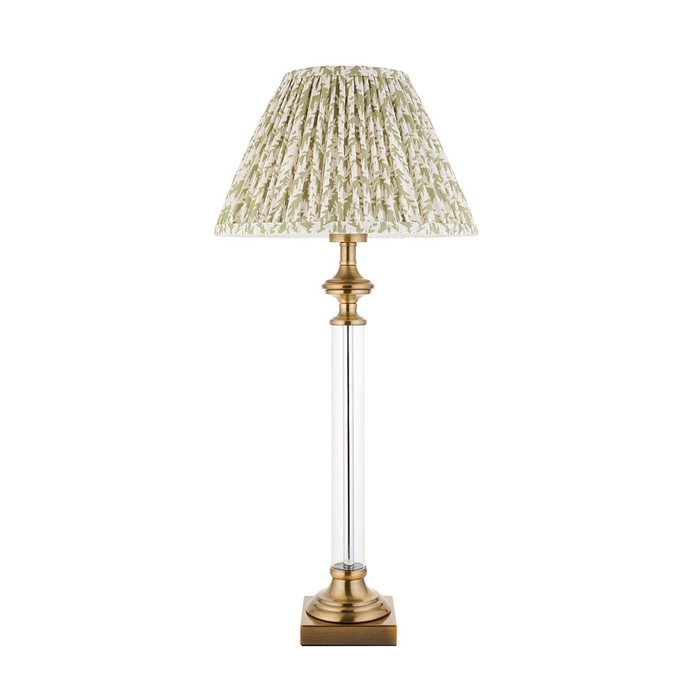 Endon Aldmont Leaf table lamp with clear glass column, antique brass base and cap, and pleated green leaf-print faux linen shade on a white background.