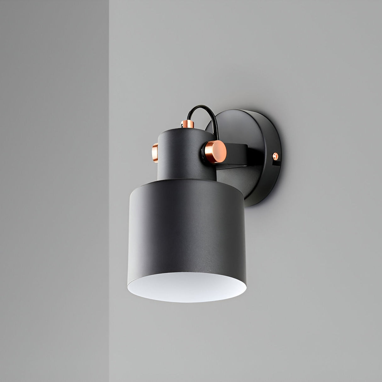 The Erika Single Spotlight in matte black with satin copper accents features a cylindrical shade, minimalist design with clean lines, and is adjustable. Mounted on a light gray wall, it provides a modern touch.