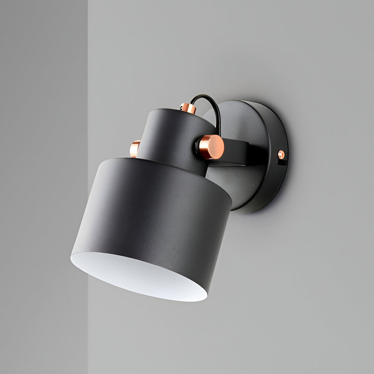 The Erika Single Spotlight in matte black and satin copper is a modern wall-mounted light featuring a downward-angled cylindrical shade, perfect as an adjustable single spotlight on a gray wall.
