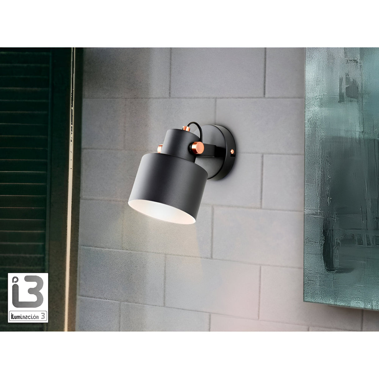 The Erika Single Spotlight in Matte Black/Satin Copper shines against a gray tiled wall, positioned next to a dark green shutter on the left and partially revealing a green abstract painting on the right.