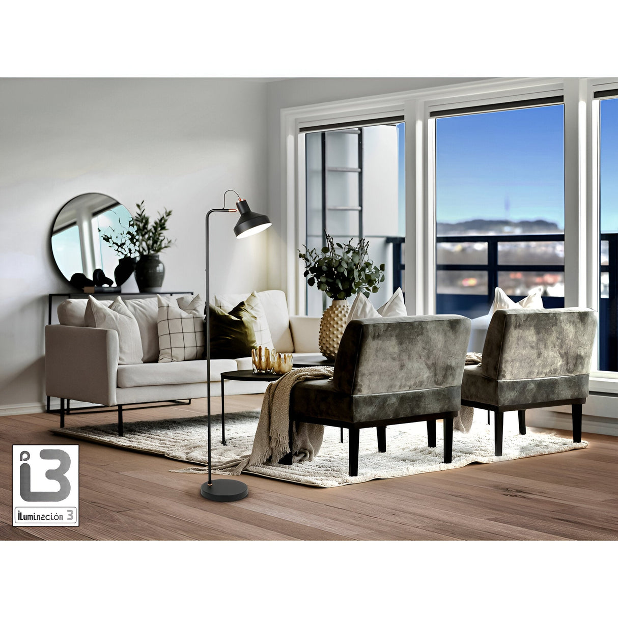 A modern living room featuring a beige sofa, two gray armchairs, the Irias Floor Lamp in matte black/copper, a round mirror, plants, and large windows opening to a balcony with blue sky. “Iluminación 3” logo appears at the bottom left.