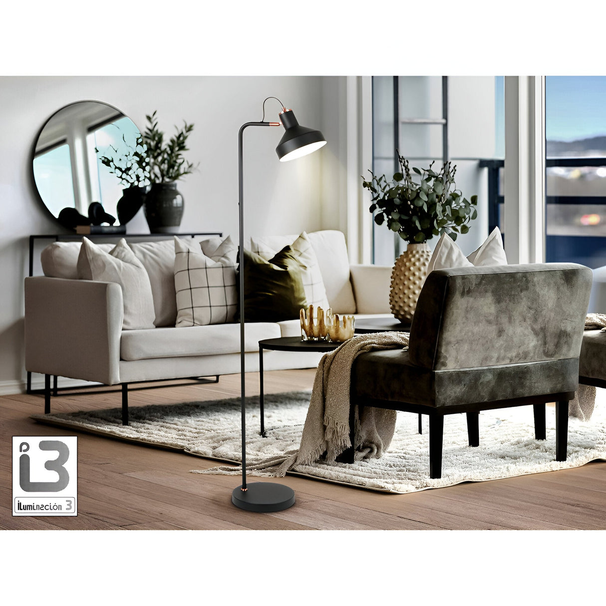 Modern living room with a beige sofa, green velvet chair, coffee table, and the Irias Floor Lamp in Matte Black/Copper. Decor features plants, vases, pillows, large windows for natural light, and a round mirror on a console behind the sofa.